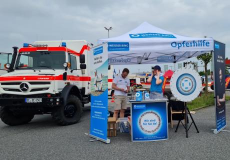 Stand 2 Mitarbeiter, eine Mitarbeiterin hält sich die Ohren zu und lacht wegen der zum Startschuss aufheulenden Sirenen, der andere Mitarbeiter hält Trillerpfeifen in der Hand und schaut nach unten